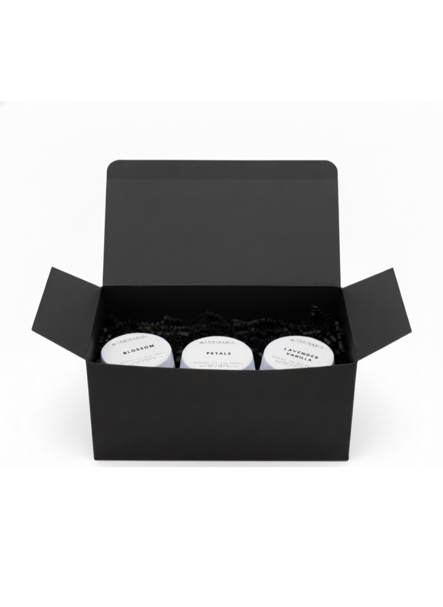 Open black gift box containing three white 2 oz candles in tins labelled Blossom, Petals and Lavender Vanilla on a white background.