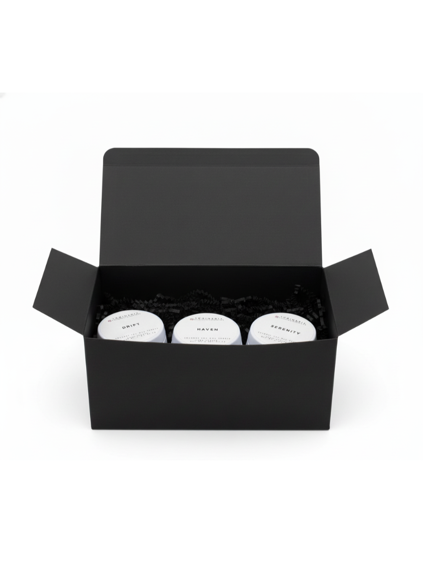Open black gift box containing three white 2 oz candles in tins labelled Drift, Haven and Serenity on a white background.