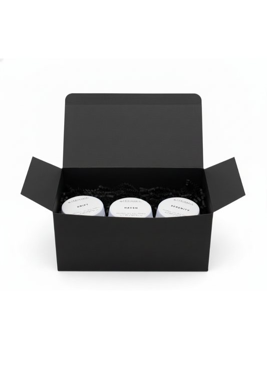 Open black gift box containing three white 2 oz candles in tins labelled Drift, Haven and Serenity on a white background.