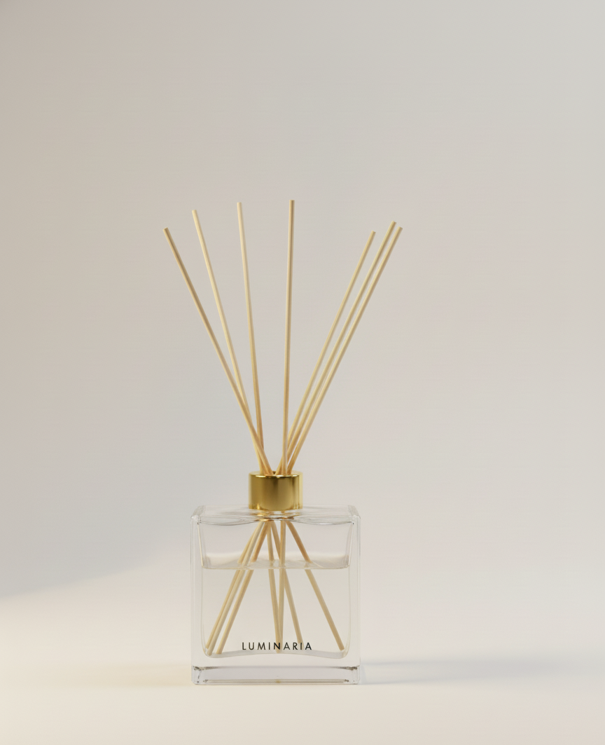 Clear glass reed diffuser bottle with a gold cap and long gold sticks emerging, set against a light beige background.